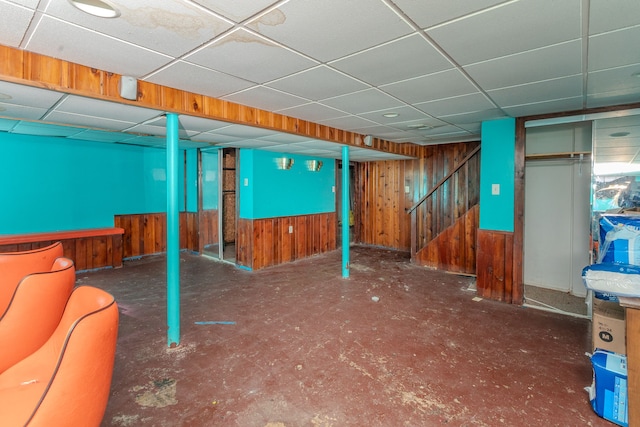 basement featuring a drop ceiling and wood walls