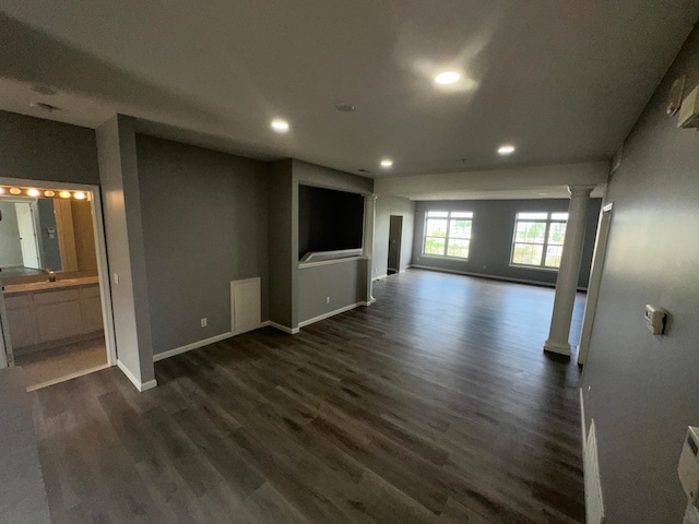 unfurnished living room with decorative columns, dark wood-type flooring, and sink