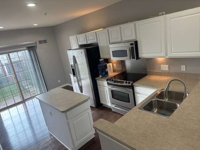 kitchen with appliances with stainless steel finishes, sink, a center island, white cabinetry, and lofted ceiling