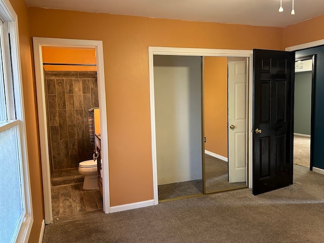 unfurnished bedroom featuring multiple windows, carpet floors, ensuite bath, and a closet