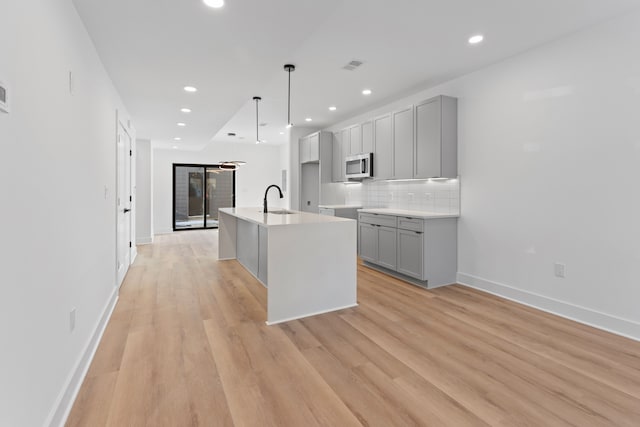 kitchen featuring sink, gray cabinets, decorative backsplash, a center island with sink, and light wood-type flooring