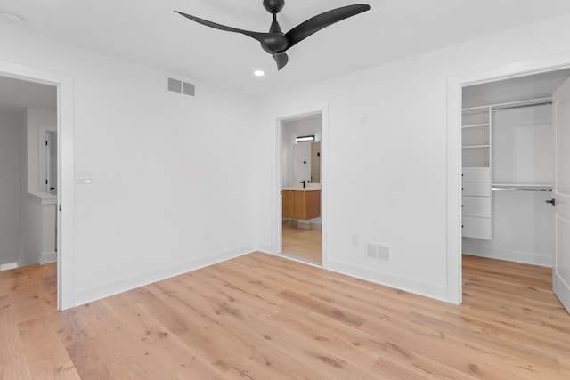 unfurnished bedroom featuring ceiling fan, a walk in closet, light wood-type flooring, and a closet