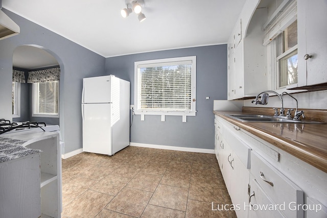 kitchen featuring white cabinets, light tile patterned floors, white fridge, and sink