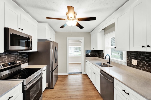 kitchen with appliances with stainless steel finishes, backsplash, sink, light hardwood / wood-style flooring, and white cabinets