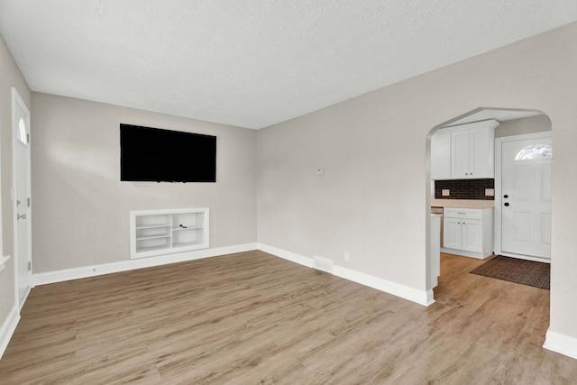 unfurnished living room with a textured ceiling, light wood-type flooring, and built in shelves