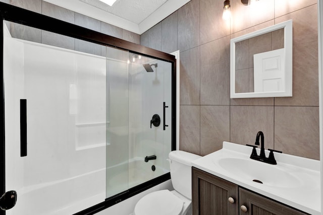 full bathroom with a textured ceiling, vanity, shower / bath combination with glass door, tile walls, and toilet