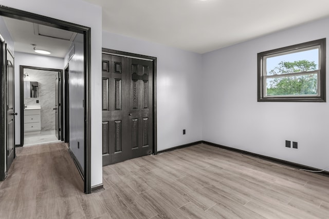 unfurnished bedroom featuring ensuite bath, light hardwood / wood-style floors, and a closet