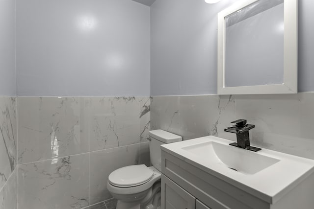 bathroom with vanity, toilet, and tile walls