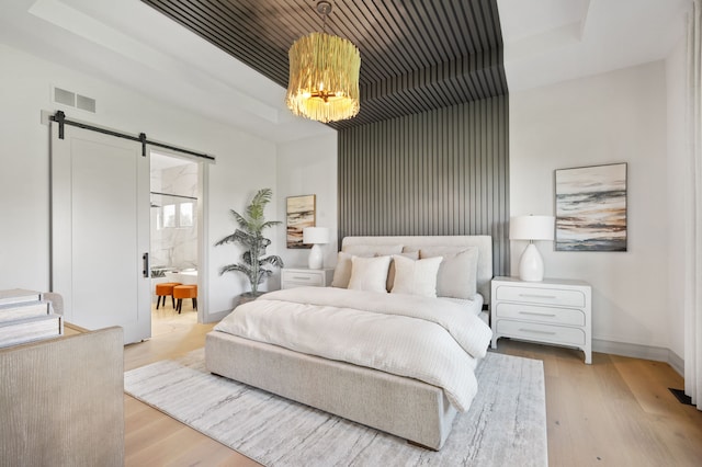 bedroom with light wood-type flooring, a barn door, ensuite bathroom, and an inviting chandelier