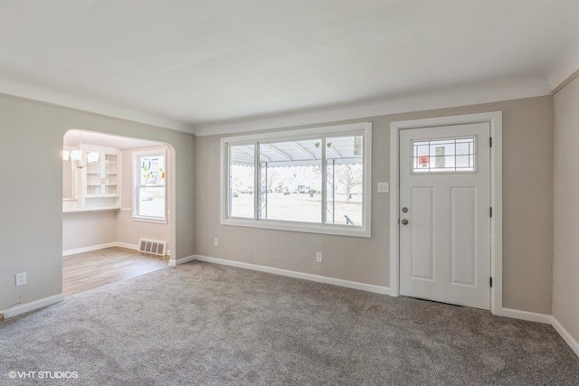 carpeted entryway featuring a notable chandelier, ornamental molding, and a wealth of natural light