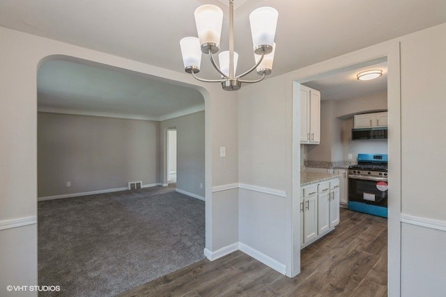 kitchen with stainless steel gas stove, white cabinetry, hanging light fixtures, and dark wood-type flooring