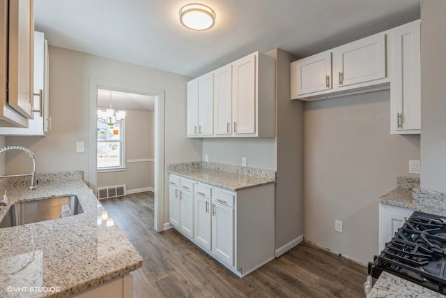 kitchen with gas stove, white cabinetry, sink, light stone counters, and dark hardwood / wood-style floors