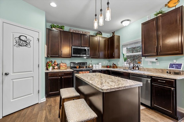 kitchen with pendant lighting, a breakfast bar, light hardwood / wood-style flooring, a kitchen island, and stainless steel appliances