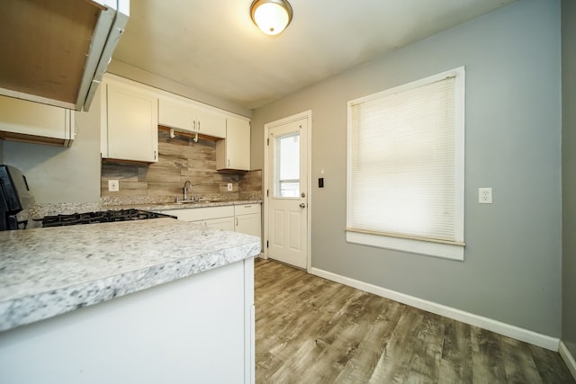 kitchen with backsplash, sink, white cabinetry, wood-type flooring, and black range with gas cooktop