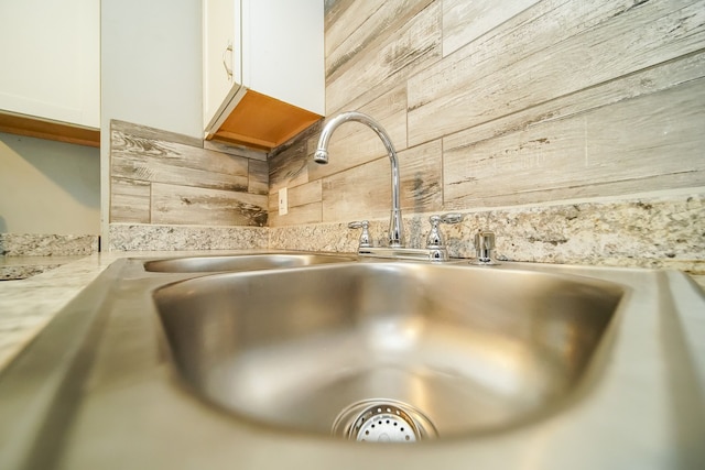 interior details featuring white cabinets, light stone counters, sink, and wooden walls