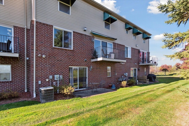 back of property with a yard, central AC, brick siding, and a balcony