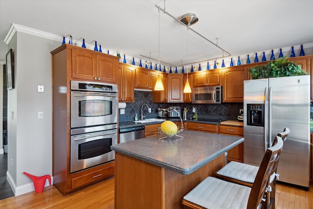 kitchen featuring light wood finished floors, stainless steel appliances, dark countertops, decorative backsplash, and a sink