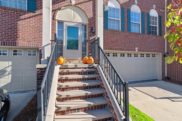 doorway to property with a garage, brick siding, and driveway