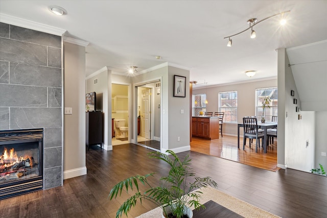 living area featuring visible vents, baseboards, ornamental molding, dark wood-style floors, and a tiled fireplace