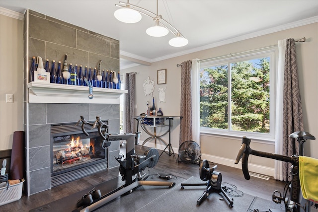 exercise area with baseboards, a tiled fireplace, wood finished floors, and crown molding