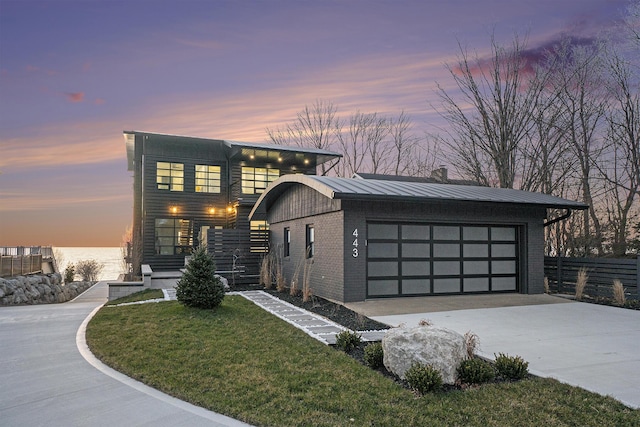 modern home featuring a water view, a garage, and a lawn