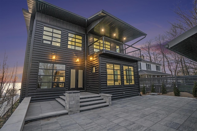 back house at dusk with french doors, a balcony, and a patio area