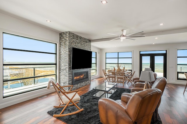 living room featuring a stone fireplace, ceiling fan, plenty of natural light, and wood-type flooring