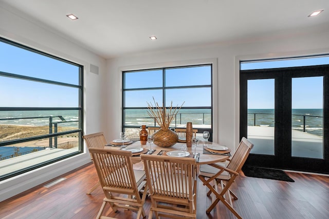 dining area featuring a water view, wood-type flooring, french doors, and a view of the beach