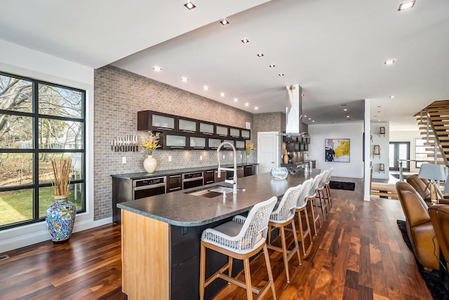 kitchen with a kitchen bar, sink, an island with sink, and dark wood-type flooring