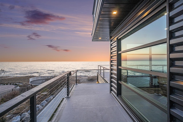 balcony at dusk featuring a water view