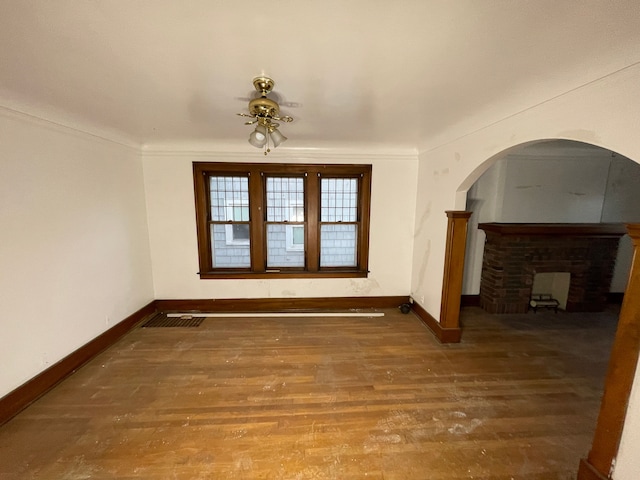 unfurnished living room with hardwood / wood-style flooring, ornamental molding, and a brick fireplace