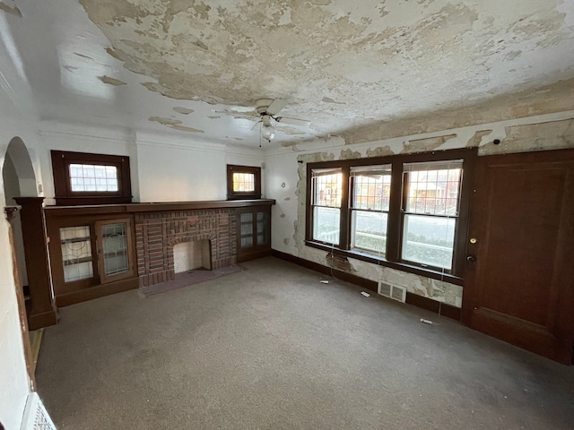 unfurnished living room with plenty of natural light, ceiling fan, carpet floors, and a fireplace