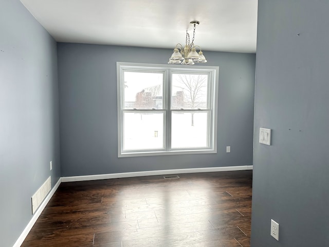 spare room featuring an inviting chandelier and dark hardwood / wood-style floors