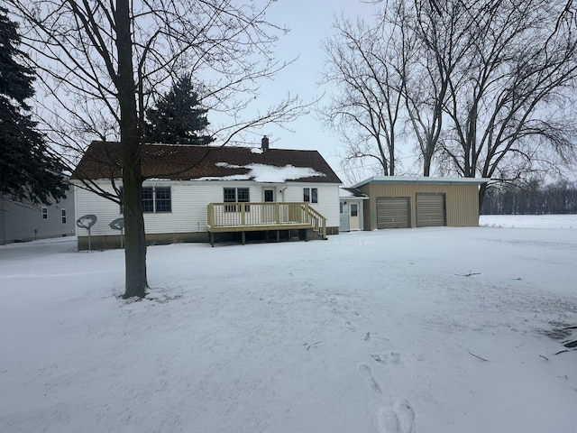 snow covered rear of property with a deck, a garage, and an outdoor structure