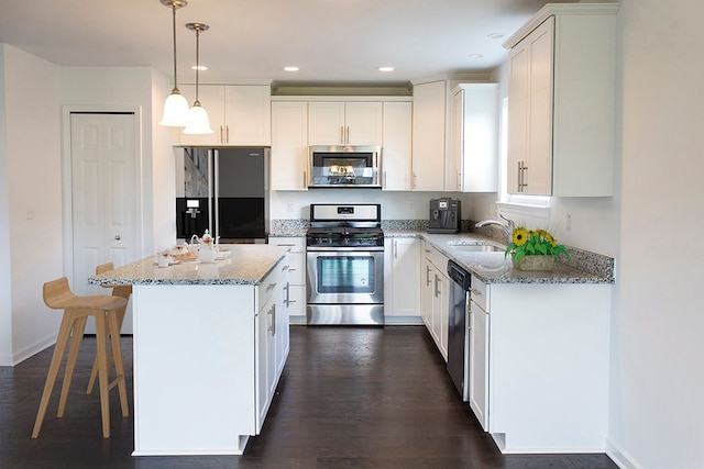 kitchen featuring light stone countertops, appliances with stainless steel finishes, a kitchen island, decorative light fixtures, and white cabinetry