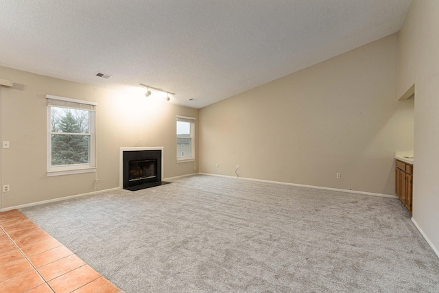 4980 Oak Hill Dr Unit 66, Waterford, MI 48329 - unfurnished living room with light colored carpet, rail lighting, a textured ceiling, and a fireplace with flush hearth