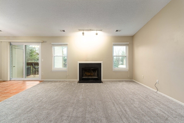 unfurnished living room with plenty of natural light, a textured ceiling, light carpet, and track lighting