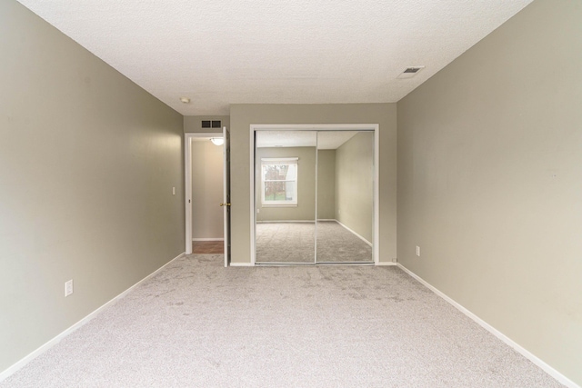 unfurnished bedroom with light colored carpet, a textured ceiling, and a closet