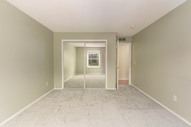 unfurnished bedroom featuring light colored carpet, a textured ceiling, and a closet