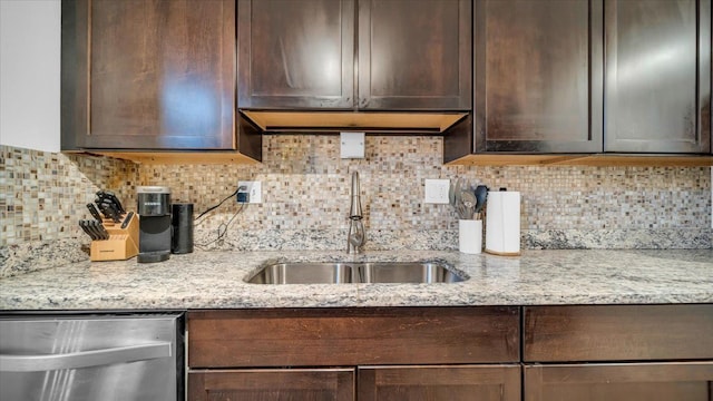 kitchen with backsplash, light stone counters, stainless steel dishwasher, dark brown cabinetry, and sink