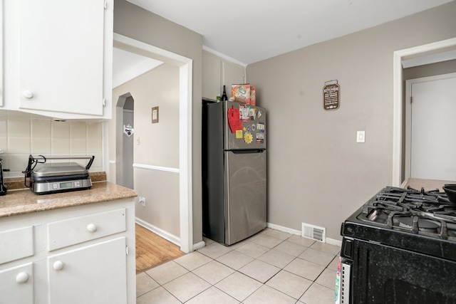 kitchen featuring tasteful backsplash, black range with gas cooktop, light tile patterned floors, white cabinets, and stainless steel refrigerator