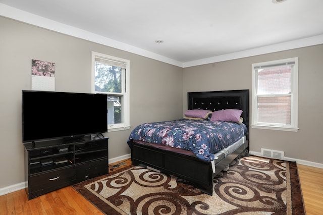 bedroom with hardwood / wood-style floors, ornamental molding, and multiple windows