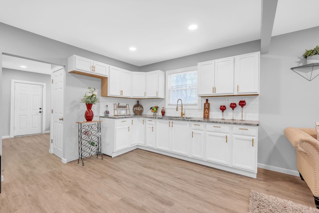 kitchen with light wood-type flooring, white cabinetry, and sink