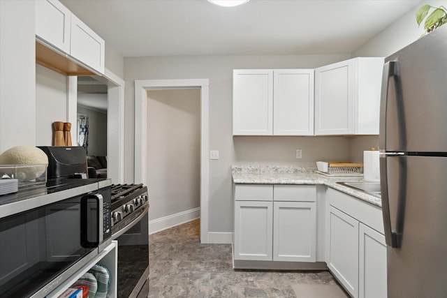 kitchen with stainless steel appliances, white cabinetry, and light stone counters