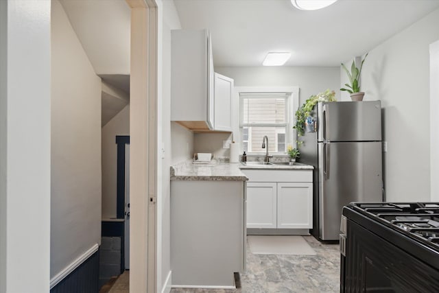 kitchen with stainless steel fridge, white cabinetry, sink, and stove