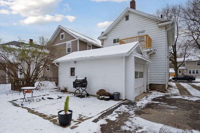 snow covered back of property featuring a balcony and a garage