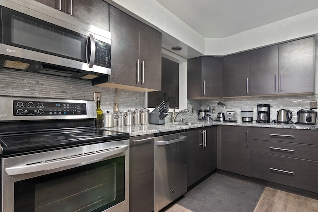 kitchen with light stone countertops, appliances with stainless steel finishes, dark hardwood / wood-style flooring, tasteful backsplash, and sink