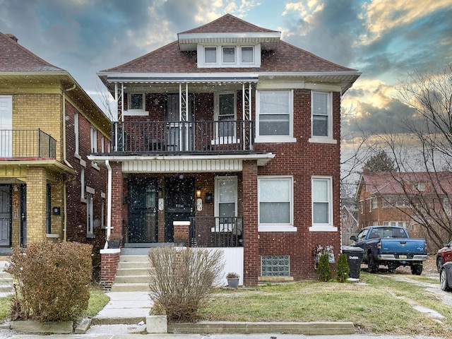 view of front of property featuring covered porch, a balcony, and a lawn