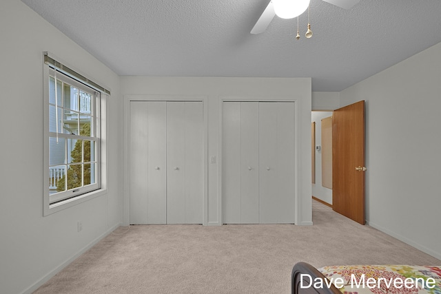 unfurnished bedroom with multiple closets, ceiling fan, light colored carpet, and a textured ceiling