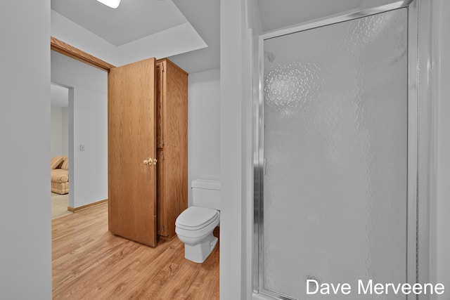 bathroom with wood-type flooring, toilet, and a shower with shower door